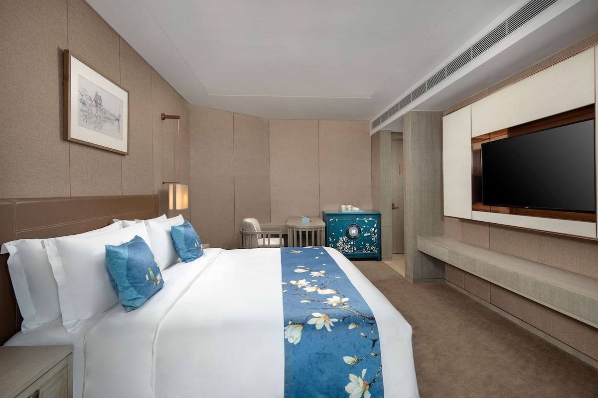 A hotel room with a large bed, a TV mounted on the wall, a desk, and a chair.