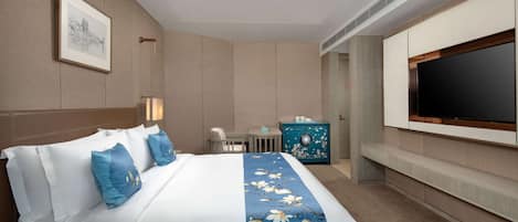 A hotel room with a large bed, a TV mounted on the wall, a desk, and a chair.
