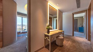 Une chambre d’hôtel moderne dotée d’un grand miroir, d’une coiffeuse agrémentée d’un vase de fleurs et offrant une vue sur la ville grâce à de grandes fenêtres.