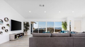 A modern living room with a large gray sectional sofa, a flat-screen TV mounted on the wall, and a sliding glass door leading to an outdoor patio.