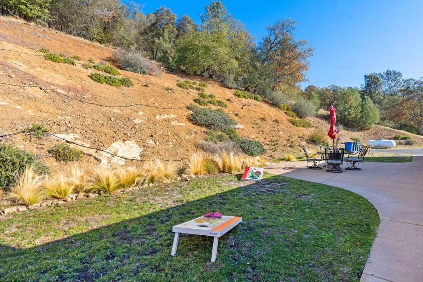 Un patio con mobiliario exterior, una mesa pequeña y un paraguas rojo.