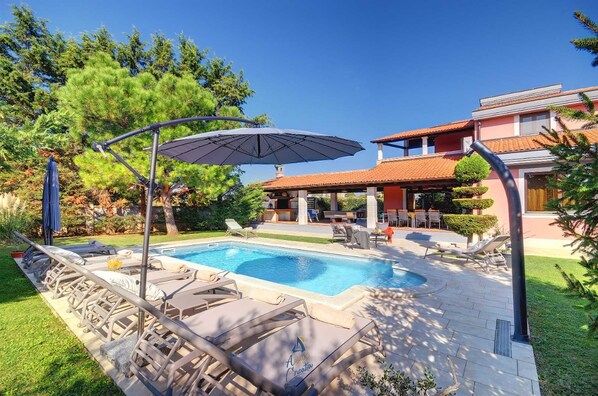 A swimming pool with lounge chairs and umbrellas, surrounded by a well-maintained lawn and trees.