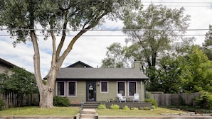 A two-story house with a front porch, a wooden fence, and a large tree in the yard.