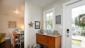 A dining area with a wooden table and chairs, a wicker basket with books, and a wall-mounted sign reading "BEACH HOUSE".