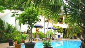 A pool area with lounge chairs and umbrellas, surrounded by potted plants and a building in the background. -  Ocean View Villa with Pool - Flamingo Beach (Playa Flamingo)