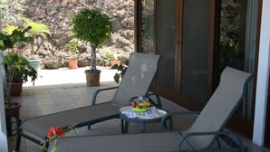 Eine Terrasse mit zwei Liegestühlen, einem kleinen Tisch mit Obstschale und mehreren Blumentöpfen.