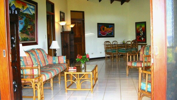 A spacious living room with a sofa, chairs, a dining table, and artwork on the walls. -  Ocean View Villa with Pool - Flamingo Beach (Playa Flamingo)