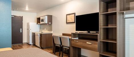 A compact hotel room with a kitchenette, a bed, a desk with a chair, and a TV.