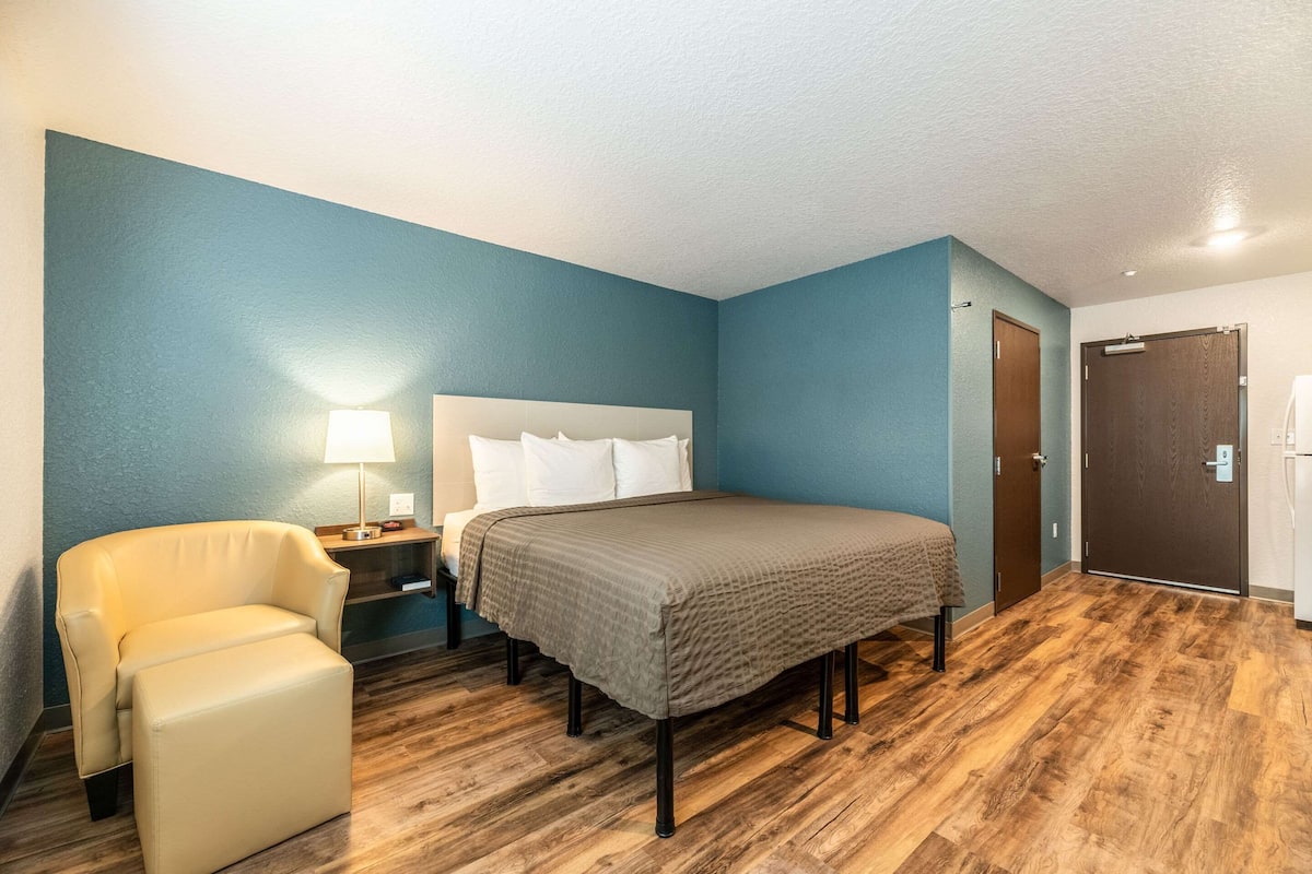 A bedroom with a bed, a chair, a nightstand, a lamp, and a door.