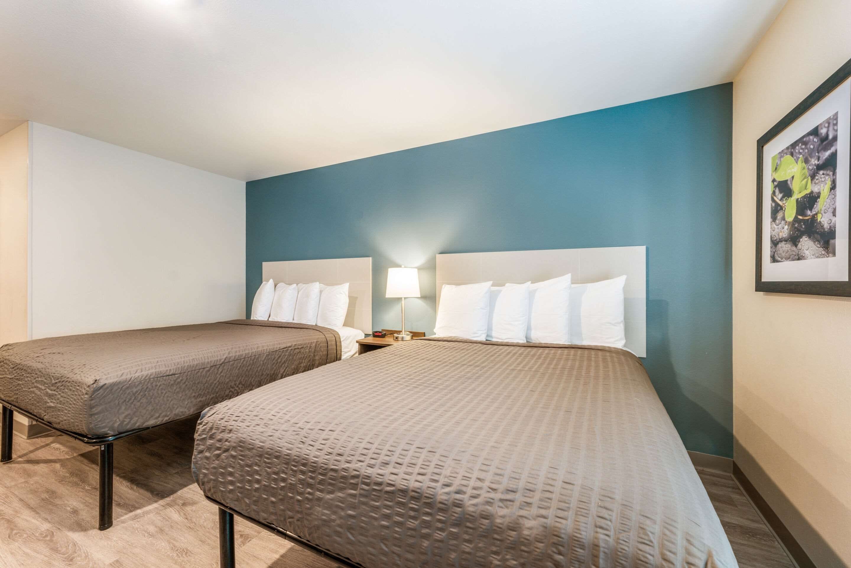 Une chambre d’hôtel avec deux lits, une table de chevet, une lampe et un tableau encadré au mur.
