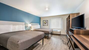 A hotel room with two beds, a TV, a desk, and a window with blinds.