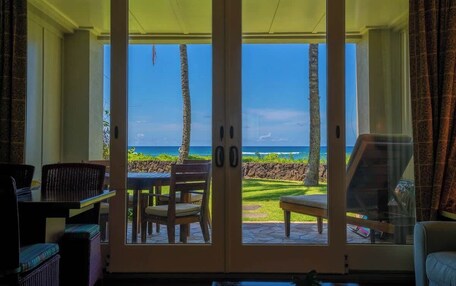 A room with a sliding glass door leading to a patio with a view of the ocean and palm trees.