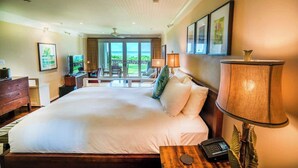 Ein geräumiges Schlafzimmer mit einem großen Bett, einem Schreibtisch mit Lampe, einem Fernseher und Blick ins Freie.