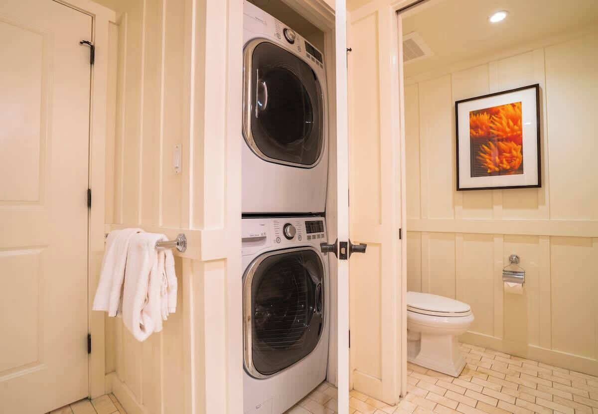 A bathroom with a double washing machine, a toilet, and a framed picture on the wall.