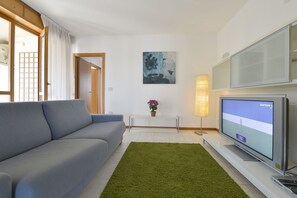 A modern living room with a grey sofa, a green rug, a flat-screen TV, a small table with a potted plant, and a painting on the wall. - UR-NEST Emilia Levante A (Bologna)