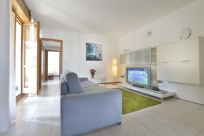 Ein modernes Wohnzimmer mit einem grauen Sofa, einem Flachbildfernseher und einem grünen Teppich.