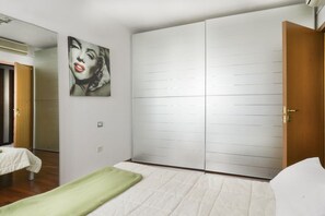 A bedroom with a bed, a green blanket, a wardrobe, and a painting on the wall. - UR-NEST Emilia Levante A (Bologna)