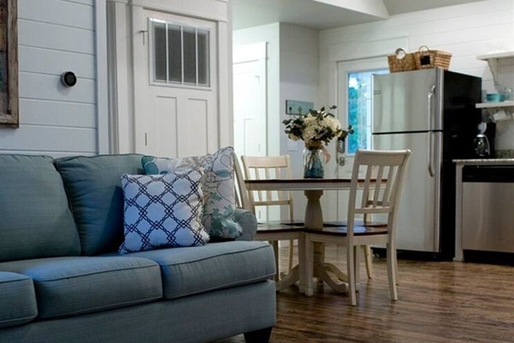 A living room with a sofa, chairs, a dining table, and a kitchen area with a refrigerator.