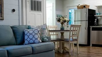 A living room with a sofa, chairs, a dining table, and a kitchen area with a refrigerator.