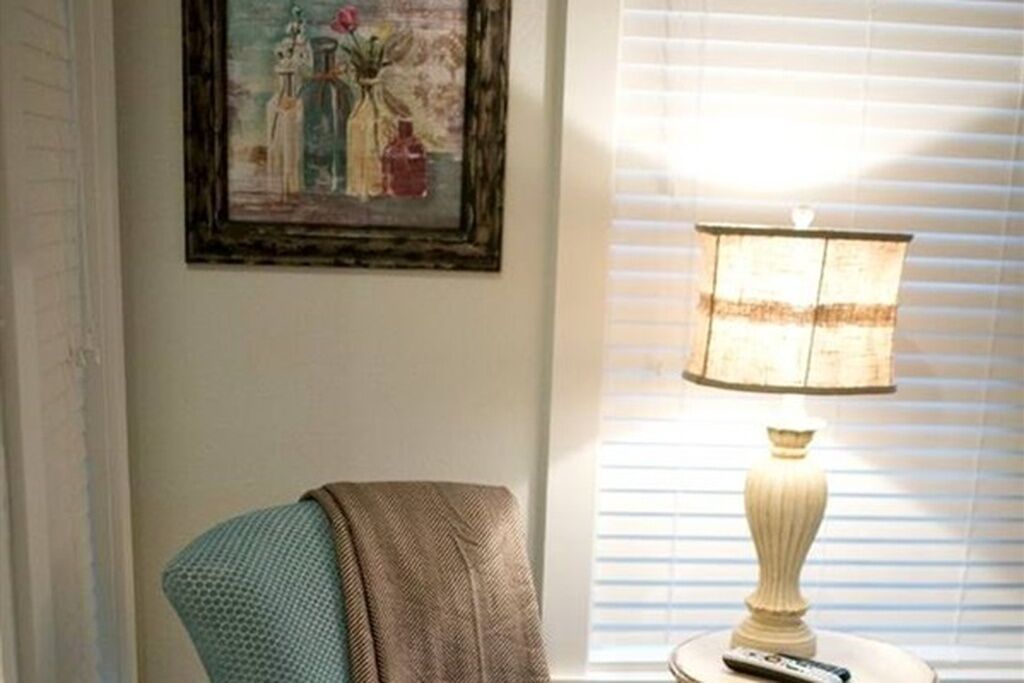 Een kamer met een enkele stoel, een lamp en een schilderij aan de muur.