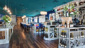 Zona de bar con suelo de madera, diferentes distribuciones de asientos y una variedad de botellas de vino exhibidas en estanterías.