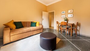 A living room with a beige sofa, a round ottoman, a dining table with chairs, and a door leading to another room. - UR-NEST Lame, Spacious one bedroom (Bologna)
