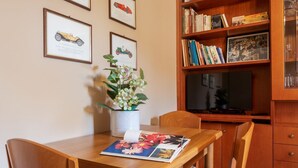 A wooden dining table with chairs, a vase with flowers, and a book. There is a bookshelf with books and framed pictures on the wall. - UR-NEST Lame, Spacious one bedroom (Bologna)