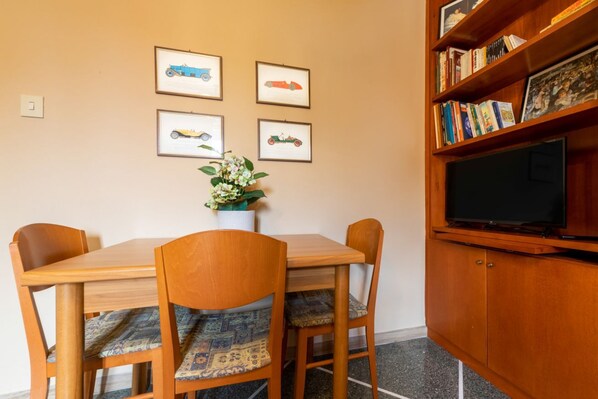 A dining area with a wooden table and chairs, a potted plant, and framed pictures on the wall.