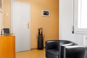 A room with a closed door, a desk with a computer, a black leather chair, and a framed picture on the wall.