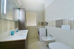 A modern bathroom with a white sink, a bidet, a washing machine, and a mirror. - UR-NEST Moline, Lovely three bedroom two bathroom apartment (Bologna)