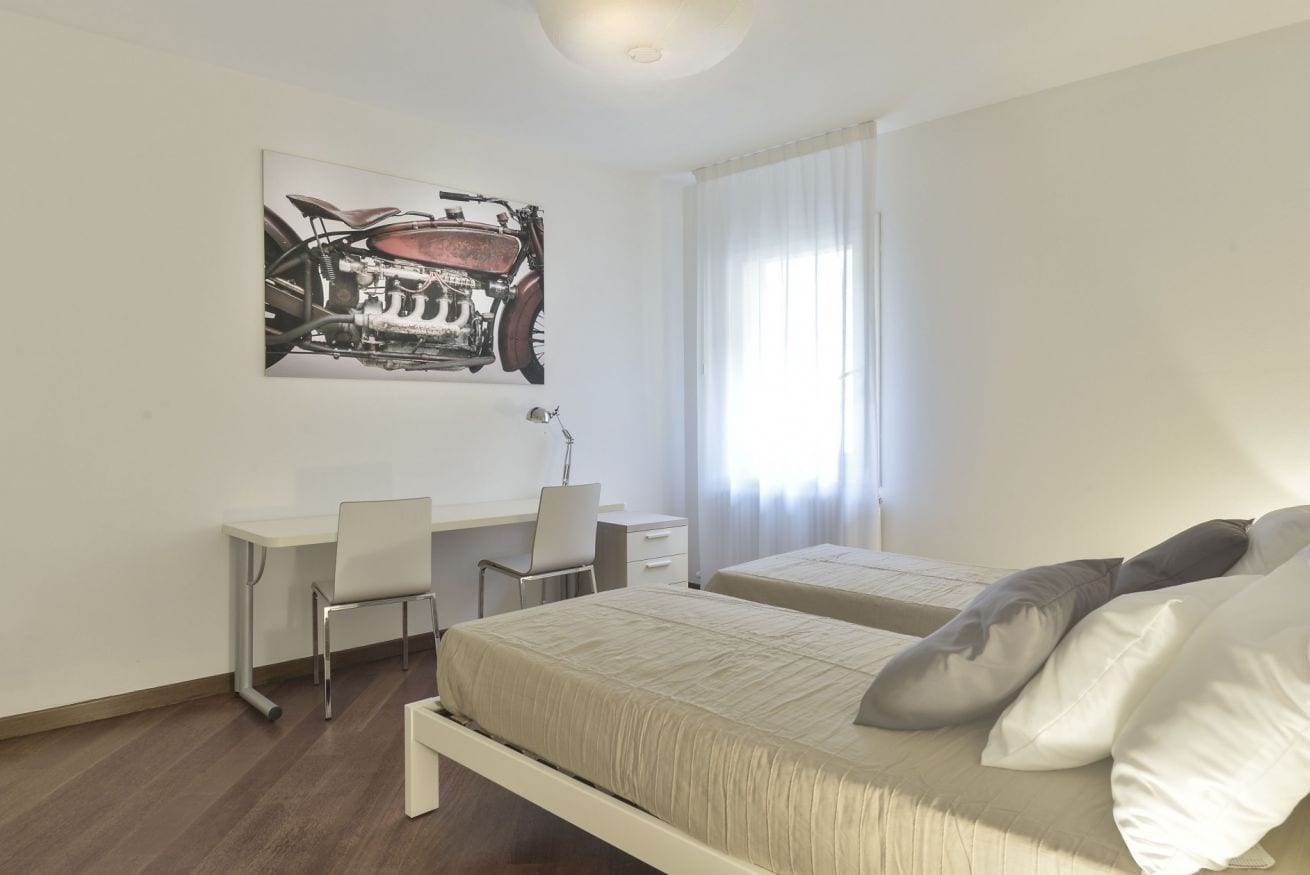 A bedroom with a bed, two bedside tables, a desk, and a chair.