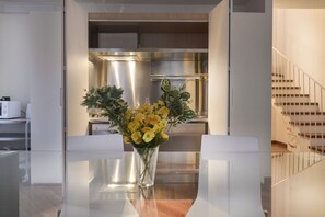 Una cucina moderna con elettrodomestici in acciaio inossidabile e un'area pranzo con un tavolo in vetro trasparente e sedie bianche.