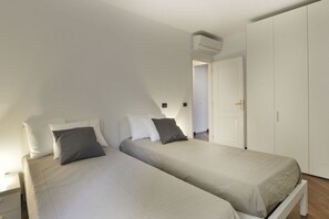 A bedroom with two beds, white walls, a white wardrobe, and a door leading to another room. - UR-NEST Moline, Stunning Apartment (Bologna)