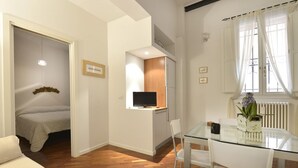 Un espacio habitable compacto con una cama, una kitchenette pequeña, una mesa de comedor de vidrio y un televisor.