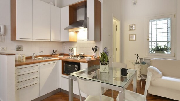 Una cocina moderna con armarios blancos, encimera de madera y mesa de comedor de vidrio.