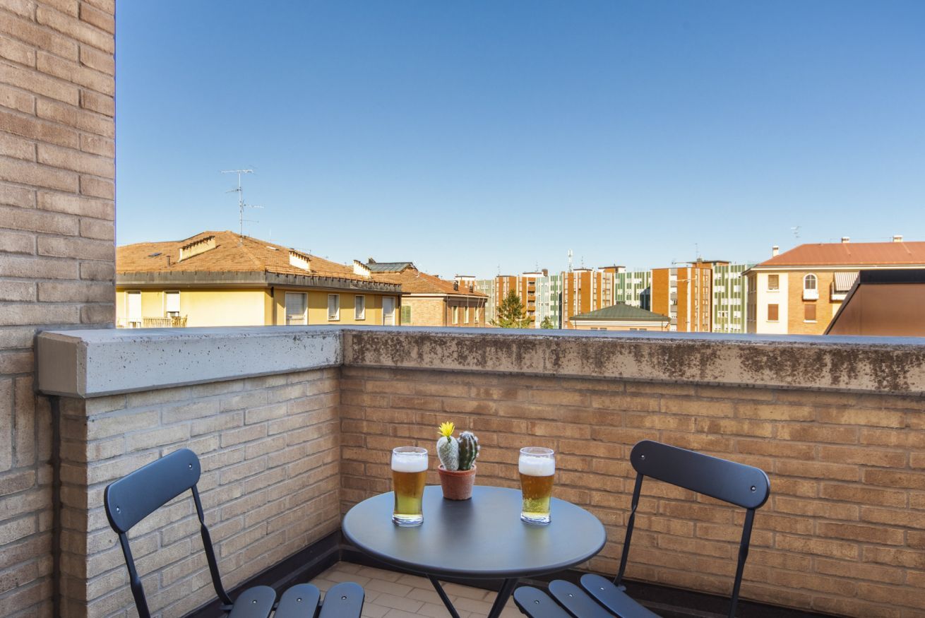Un balcone con due sedie, un tavolino, due bicchieri di birra e una pianta di cactus.