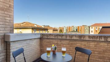 Un balcone con due sedie, un tavolino, due bicchieri di birra e una pianta di cactus.