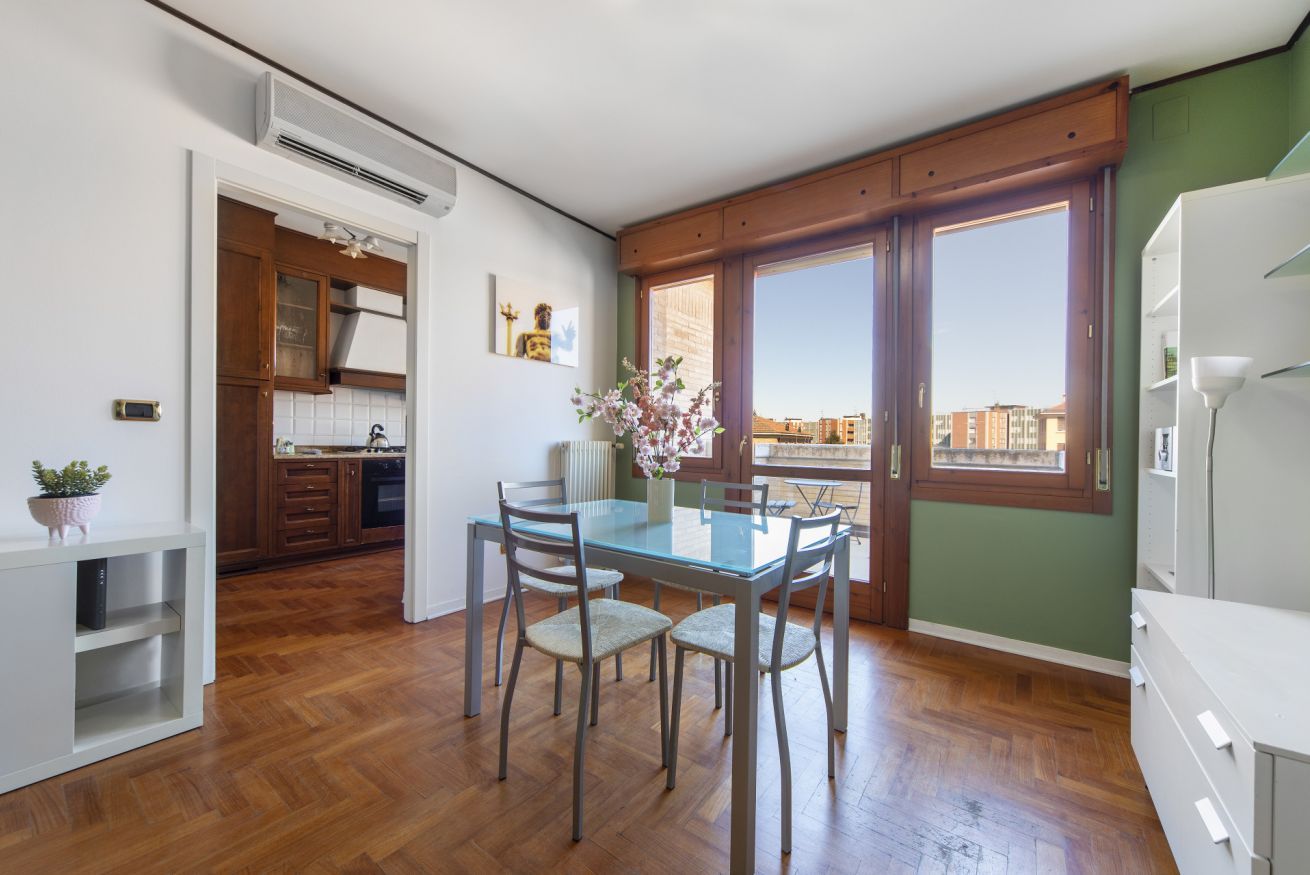 Una cucina compatta con mobili in legno, un tavolo da pranzo con sedie e un'ampia finestra con vista sulla città.