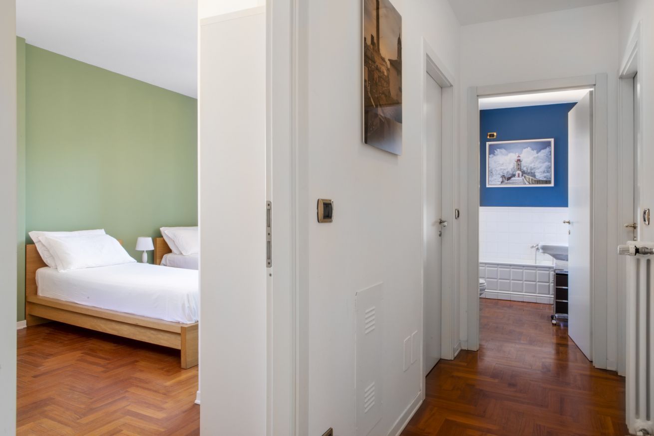 Una stanza con un letto, un comodino, una lampada a parete e una porta che dà su un'altra stanza.