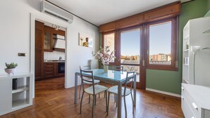 A compact kitchen with wooden cabinets, a dining table with chairs, and a large window offering a city view. - UR-NEST Saffi, Silent and very sunny 90 sqm (Bologna)