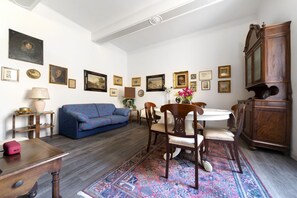 A living room with a blue sofa, wooden dining table, chairs, and a patterned rug. - UR-NEST Fusari, Wonderful apartment  (Bologna)