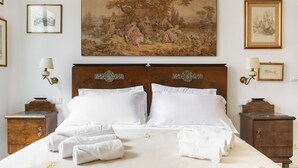 Un lit bien fait, avec du linge de lit et des serviettes blanches, un grand tableau représentant un paysage au-dessus, et deux tables de chevet avec des lampes.