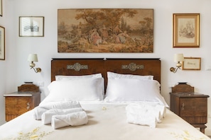 A neatly made bed with white linens and towels, a large landscape painting above it, and two bedside tables with lamps. - UR-NEST Fusari, Wonderful apartment  (Bologna)