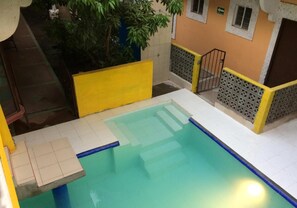 A swimming pool with a yellow and white tiled deck, surrounded by a low fence and a small staircase leading to a door. - Hotel Quinta San Juan (Ciudad Valles)