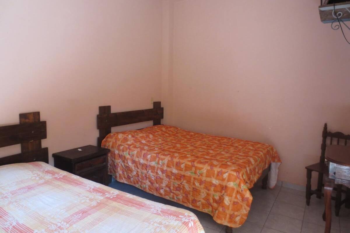 A small, simple room with two single beds, a wooden nightstand, a chair, and a desk.