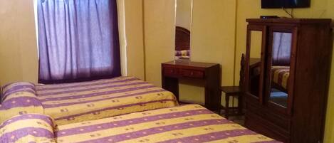 A room with two beds, a desk, a mirror, a television, and a wardrobe.