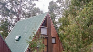 A rustic wooden cabin with a sloped roof, a small deck, and a window with shutters. - Junction Retreat - Ohakune Holiday Home (Ohakune)