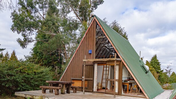 A wooden A-frame cabin with a deck, a picnic table, and a ladder leading to the entrance. - Junction Retreat - Ohakune Holiday Home (Ohakune)