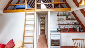 A loft bedroom with a wooden ladder, a bunk bed, and a kitchenette. - Junction Retreat - Ohakune Holiday Home (Ohakune)