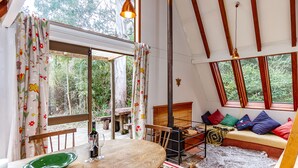 A cozy, naturally lit room with a wooden dining table, a bench, and a sofa with colorful cushions. - Junction Retreat - Ohakune Holiday Home (Ohakune)